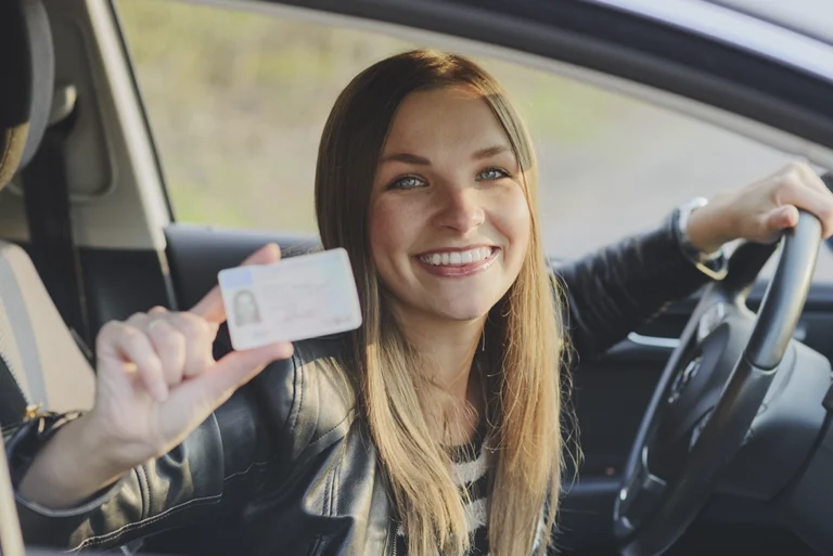 Joven sonriente mostrando su licencia de conducir permanente en el auto tras pasar el examen