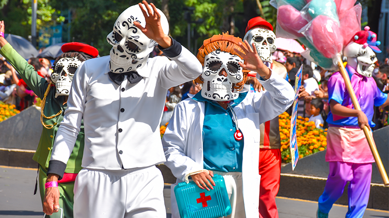 Personas vestidas de calaveras con traje de médicos que desfilan en el Mega Desfile de Día de Muertos en la CDMX