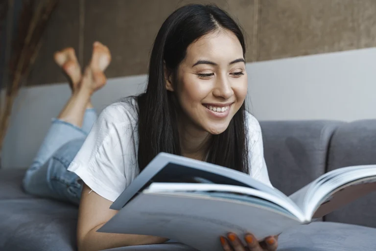 Joven universitario sonriente leyendo un libro en su casa, representando cómo la lectura mejora el aprendizaje y el rendimiento académico de forma natural