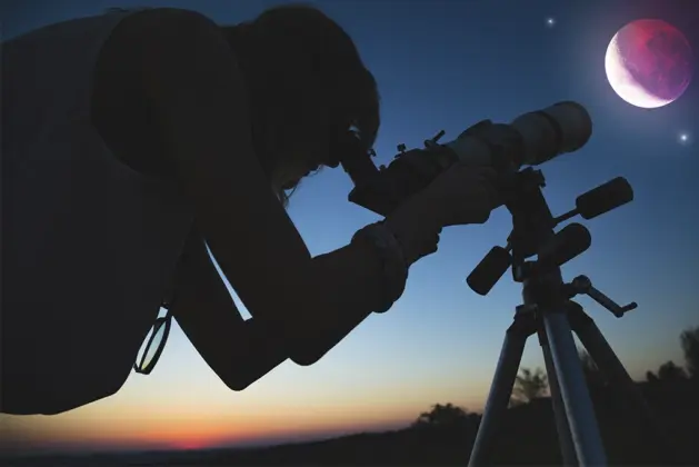 Sombra de un joven mirando en su telescopio el eclipse total de luna