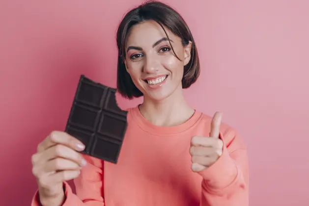 oven estudiante sonriente comiendo chocolate negro mientras estudia, representando los beneficios del chocolate para estudiar y mejorar la concentración