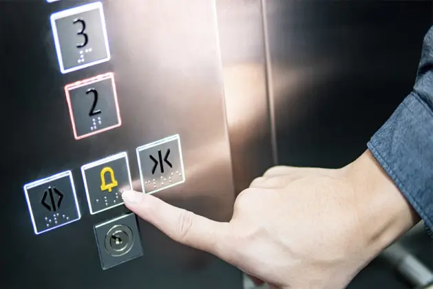 Mano presionando el botón de alarma en un elevador, representando una de las cosas a hacer al quedarse atrapado dentro de un elevador