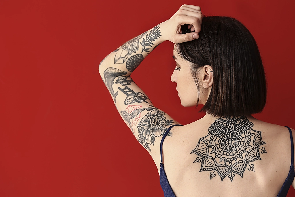 Mujer mostrando de espalda sus tatuajes con diversos estilos. Ejemplo visual de los tipos de tatuajes más populares