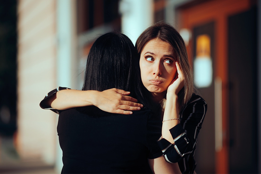 mujer abrazando a otra con mala cara, cayendo en comportamientos de amistades tóxicas.