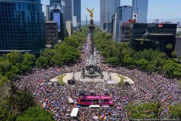 Multitud de personas diversas celebrando el Pride CDMX en 2026 frente al Ángel de la Independencia, ondeando banderas arcoíris y carteles con el lema de la marcha, en una imagen llena de color y alegría.